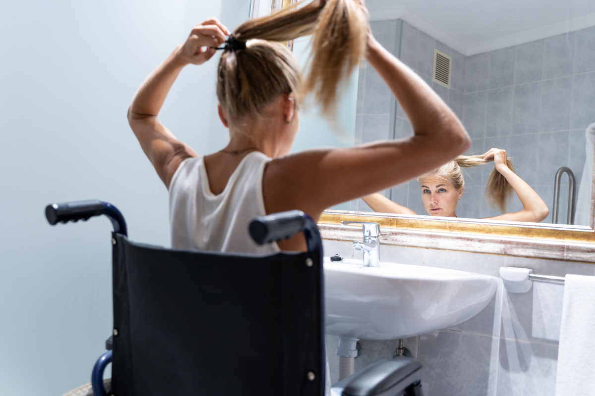 Young female wheelchair user brushing hair in accessible walk-in shower bathroom in Chichester, featuring wheelchair-friendly wash basin.